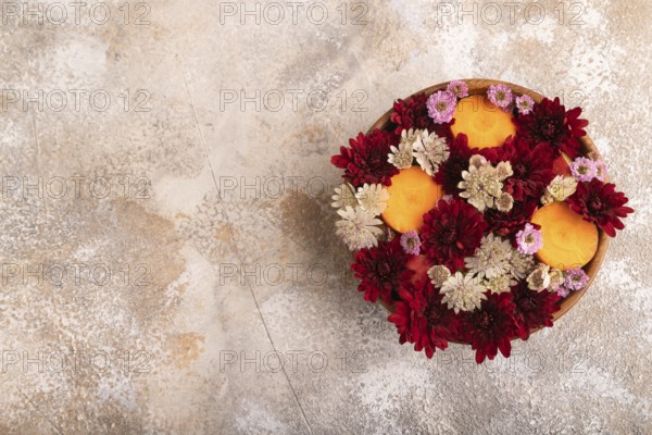 Wooden bowl with carrot slices and red Chrysanthemum flowers, Astrantia flowers, flower salad on brown concrete background, top view, flat lay, copy space, minimalism