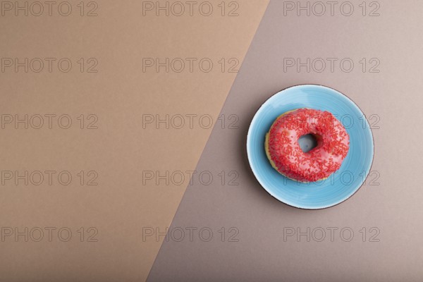 Pink Donut with sprinkles on blue ceramic plate on beige and gray pastel paper background, top view, flat lay, copy space, minimalism