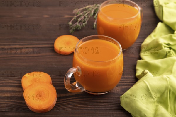 Two glasses with carrot juice, on wooden background and green textile. Diet, healthy eating concept. side view, close up, minimalism
