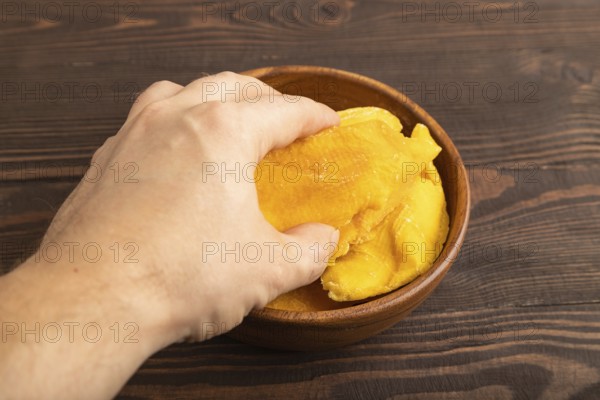 Dried Mango in wooden bowl with hand on brown wooden background. Side view, close up. healthy food, minimalism