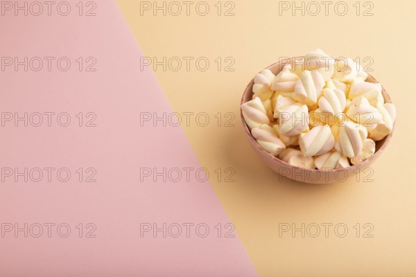 Orange and pink marshmallow in ceramic bowl on pink and orange pastel paper background, side view, copy space, minimalism