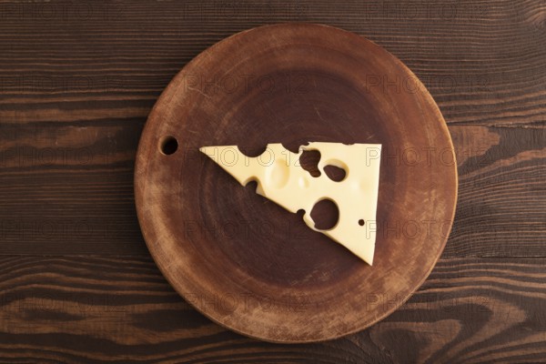 Piece of cheese with holes on cutting board on brown wooden background, top view, flat lay, copy space, minimalism