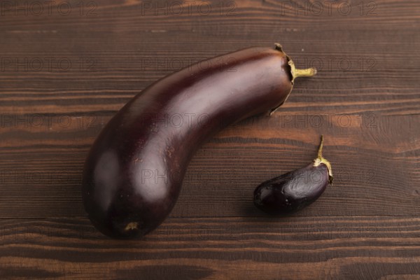 Two Eggplants big and small on brown wooden background, side view, close up, minimalism