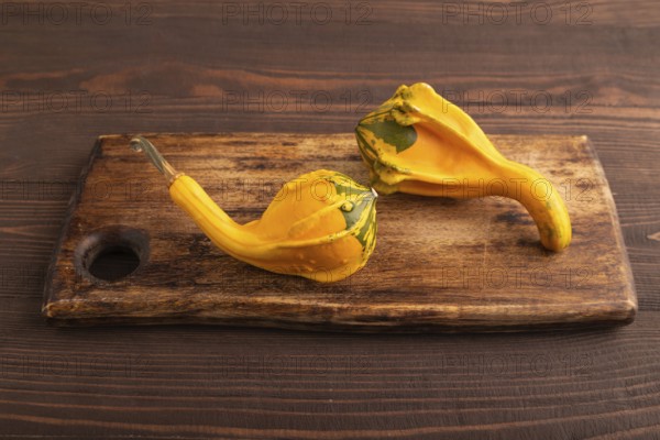 Two decorative orange Pumpkins on cutting board on brown wooden background, side view, close up, minimalism