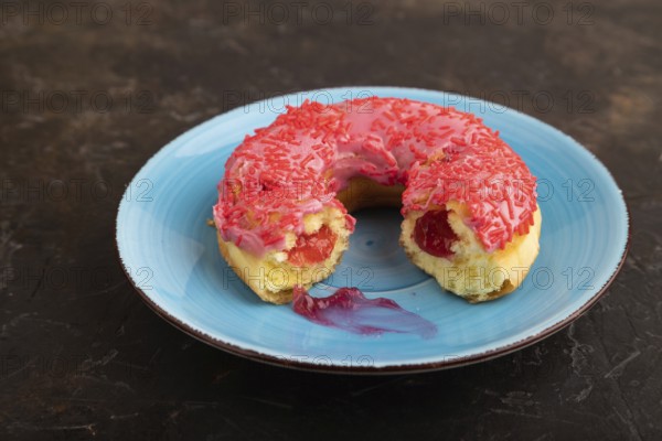 Bitten Pink Donut with sprinkles on blue ceramic plate on black concrete background, side view, close up, minimalism
