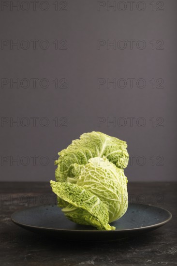 Green lettuce on blue plate on black concrete background. Side view, copy space. healthy food, vegetable, minimalism, low key