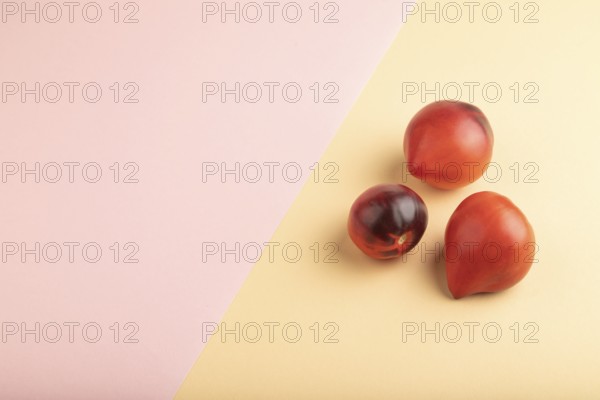 Red Heart shape tomatoes on pink and orange pastel paper background. Side view, copy space. healthy food, vegetable, minimalism
