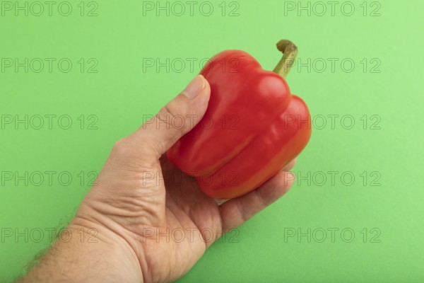 Hand holding Red pepper on green pastel background. Side view, copy space. healthy food, vegetable, minimalism