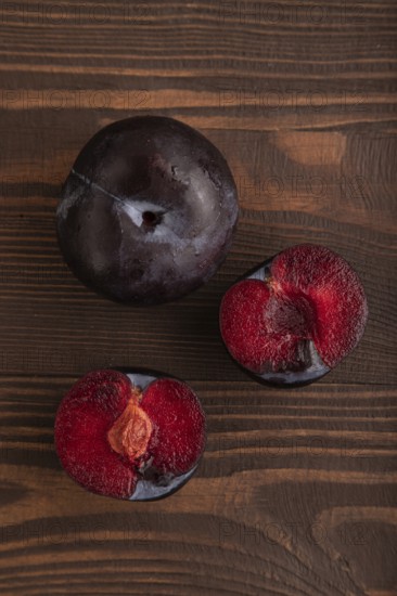 Purple Plum Cut in half on brown wooden background. Top view, flat lay, close up. healthy food, vegetable, minimalism