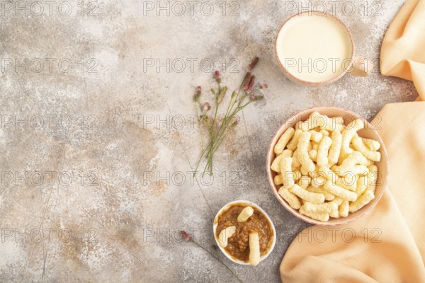 Corn flakes sticks with caramel in ceramic bowl on gray concrete background and orange linen textile. Top view, flat lay, copy space