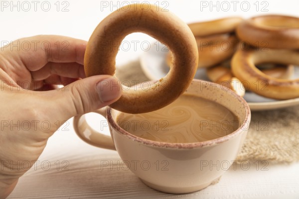 Homemade Ring Bagel with hand with cup of coffee on white wooden background and linen textile. side view, close up, selective focus