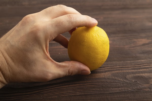 Yellow Lemon Cut in half with hand on brown wooden background. Side view, close up. healthy food, vegetable, minimalism. citrus