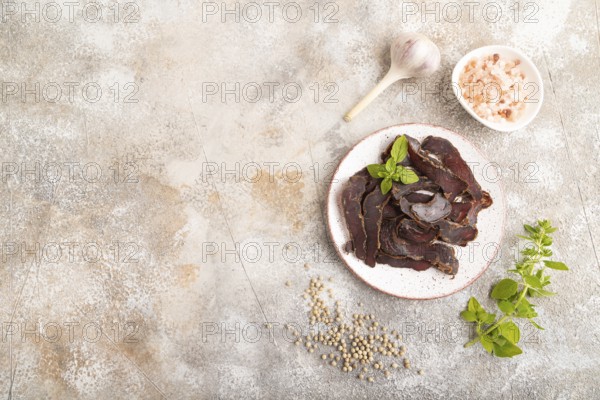 Armenian Basturma dried meat on plate with pepper and herbs on brown concrete background. Top view, flat lay, copy space