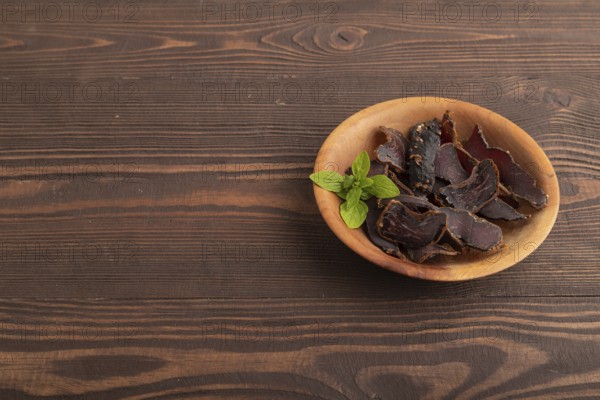 Armenian Basturma dried meat on wooden bowl with pepper and herbs on brown wooden background. Side view, copy space
