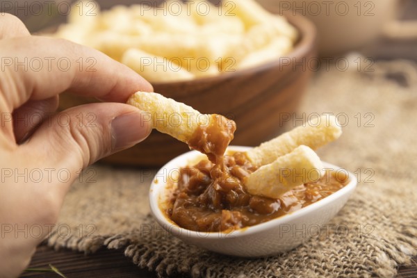 Corn flakes sticks with caramel in wooden bowl with hand on brown wooden background and linen textile. Side view, close up, selective focus