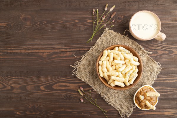Corn flakes sticks with caramel in wooden bowl on brown wooden background and linen textile. Top view, flat lay, copy space