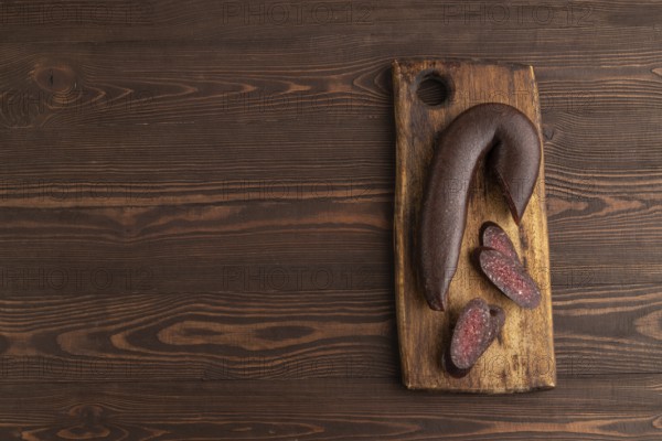 Sujuk sausage on wooden cutting board with pepper and herbs on brown wooden background. Top view, flat lay, copy space