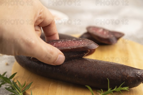 Sujuk sausage with hand on wooden cutting board with pepper and herbs on brown concrete background. Side view, close up, selective focus