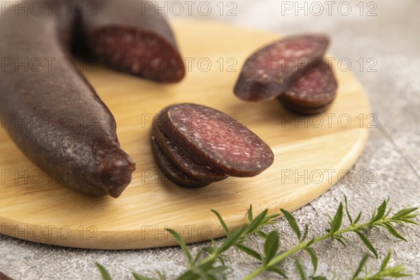 Sujuk sausage on wooden cutting board with pepper and herbs on brown concrete background. Side view, close up, selective focus