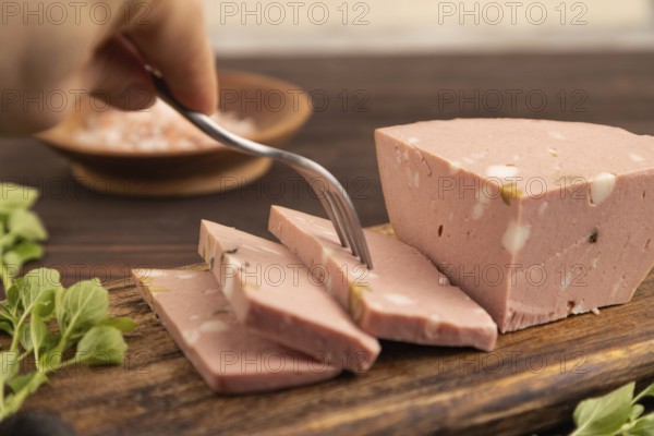 Mortadella sausage with hand on wooden cutting board with pepper and herbs on brown wooden background. Side view, close up, selective focus