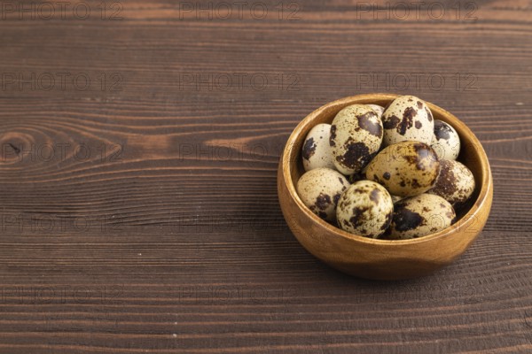 Pile of raw Quail eggs in bowl on a brown wooden background. side view, copy space