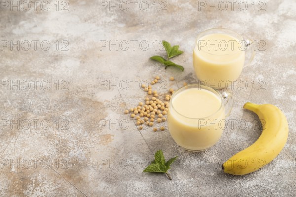 Organic non dairy banana and soy milk in glass on brown concrete background. Vegan healthy food concept, side view, copy space