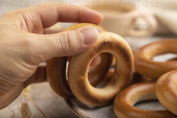 Homemade Ring Bagel with hand with cup of coffee on brown concrete background and linen textile. side view, close up, selective focus