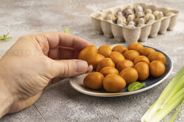 Pile of Smoked Quail eggs on plate with hand on a brown concrete background. side view, close up