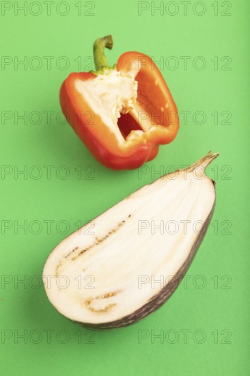 Red Cutted pepper and Purple Cutted eggplant on green pastel background. Side view, copy space. Tropical, healthy food, vegetable, slice, minimalism