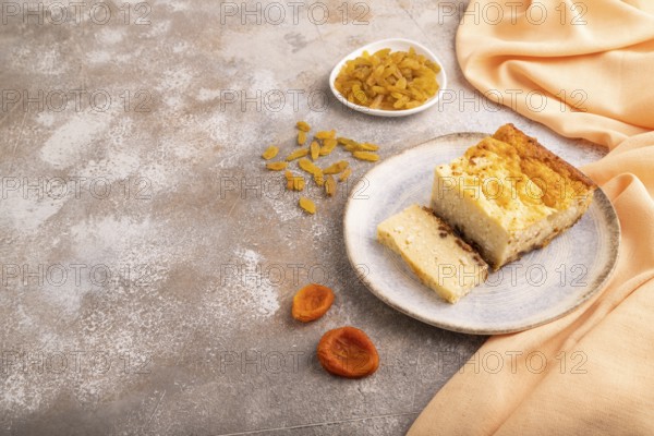 ?ottage cheese ?asserole, Curd cake, with dried apricots and raisins on brown concrete background and orange textile, side view, copy space, minimalism