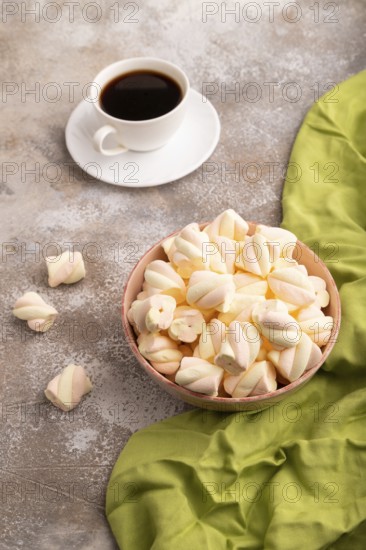 Orange and pink marshmallow in ceramic bowl on brown concrete background and green textile, side view, close up, minimalism