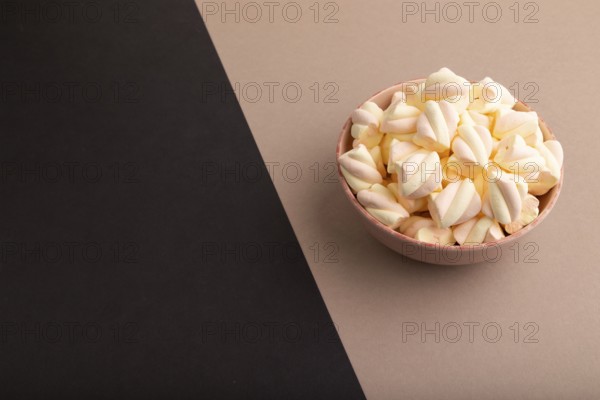 Orange and pink marshmallow in ceramic bowl on black and beige pastel paper background, side view, copy space, minimalism