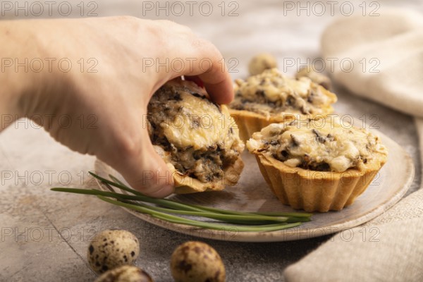 Tartlets with meat and cheese with hand on brown concrete background and linen textile. side view, close up, selective focus