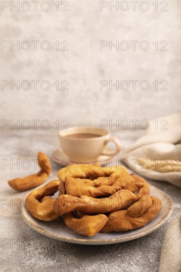 Crunchy biscuit Brushwood cookies sprinkled with powdered sugar on brown concrete background and linen textile, cup of coffee, side view, copy space
