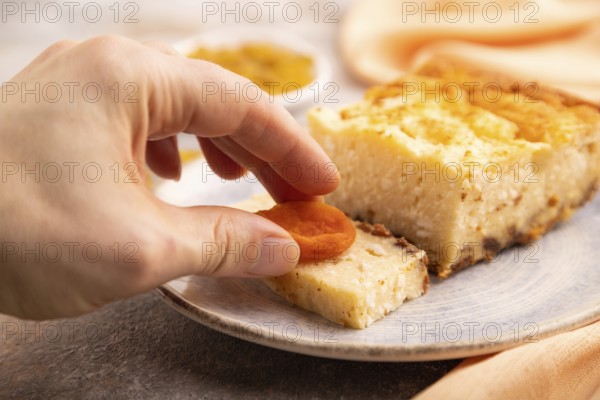 ?ottage cheese ?asserole, Curd cake, with dried apricots and raisins with hand on brown concrete background and orange textile, side view, selective focus, minimalism