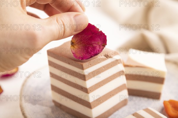Cocoa and milk jelly with dried apricots with hand on white wooden background and linen textile, side view, close up, minimalism, selective focus