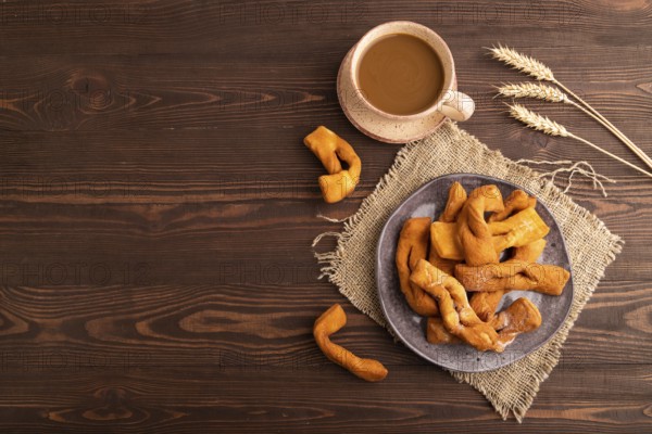Crunchy biscuit Brushwood cookies sprinkled with powdered sugar on brown wooden background and linen textile, cup of coffee, top view, flat lay, copy space