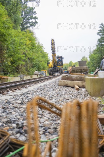 Baustelle mit Bahnschienen und Bagger in einer von Bäumen umgebenen Umgebung, sichtbar sind Metallstangen und Kies, Bau der Hermann Hessenahn, Calw, Schwarzwald, Deutschland