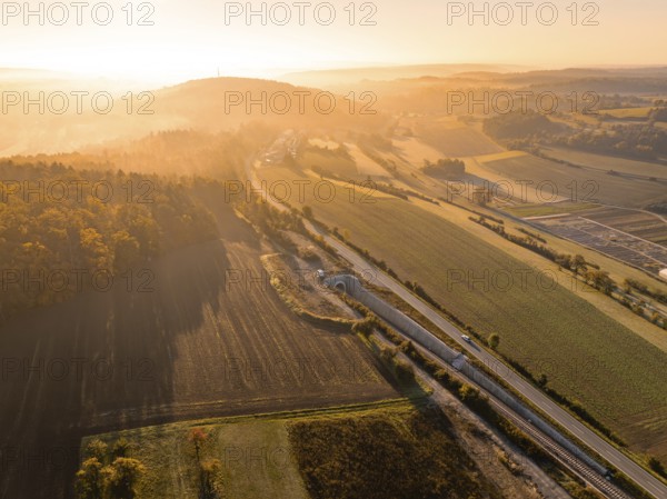 Eine von Sonnenlicht durchflutete Talansicht mit Feldern, Hügeln und Straßen bei Sonnenaufgang, Neubautunnel der Hermann Hessebahn, Calw, Schwarzwald, Deutschland