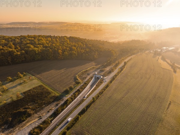 Panorama einer Landschaft in der Dämmerung mit Eisenbahn und Straße neben Feldern und bewaldeten Hügeln, Neubautunnel der Hermann Hessebahn, Calw, Schwarzwald, Deutschland