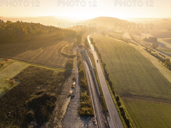 Ein Sonnenuntergang über einer ländlichen Landschaft mit Eisenbahn und Straße, umgeben von Feldern und Hügeln, Neubautunnel der Hermann Hessebahn, Calw, Schwarzwald, Deutschland