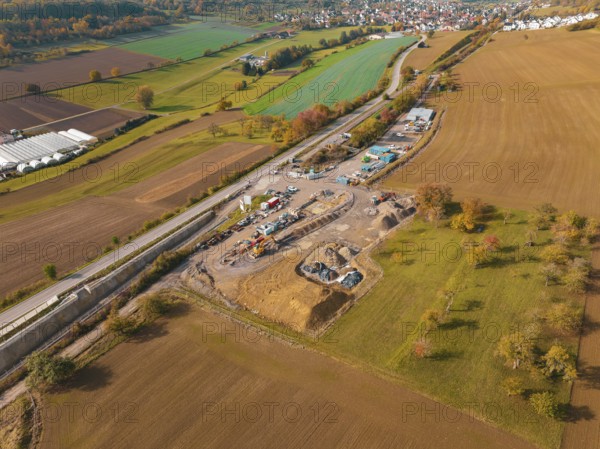 Herbstliche Luftaufnahme einer ländlichen Gegend mit einer Baustelle neben bewirtschafteten Feldern und einem Dorf in der Ferne, Neubautunnel der Hermann Hessebahn, Calw, Schwarzwald, Deutschland