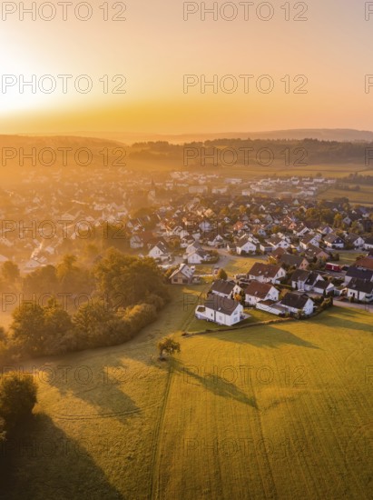 Luftaufnahme eines Dorfs bei Sonnenuntergang mit Feldern und Bäumen in warmen Orangetönen, Gechingen, Heckengäu, Landkreis Calw, Deutschland