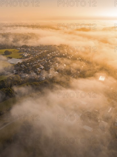 Vernebelte Luftaufnahme eines Dorfs in der Morgendämmerung in warmem Orange und Braun, Gechingen, Heckengäu, Landkreis Calw, Deutschland