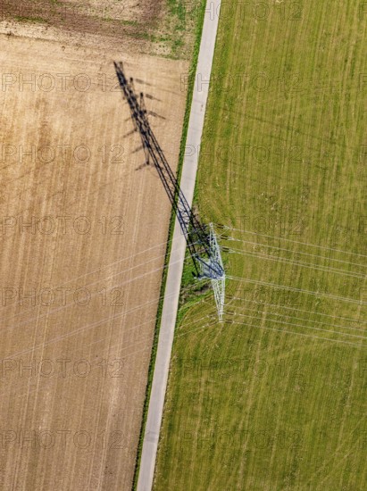Strommast thront zwischen Acker und Wiese, mit einem langen Schatten der sich über das Feld erstreckt, Nagold, Schwarzwald, Deutschland