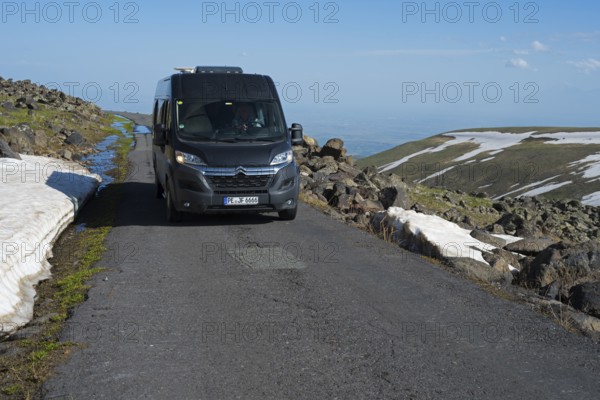 Van fährt auf asphaltiertem Weg neben Felsen und Schneefeldern mit klarem Himmel, das Tal im Hintergrund, mit dem Camper zum Aragaz, Aragats, Aragac, Alagyaz, erloschener Schichtvulkan, 4090 m, Aragazotn, Schirak, Armenien