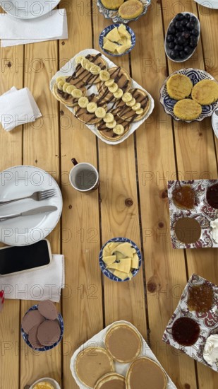 Moroccan breakfast spread with a variety of sweet and savory dishes. Including msemmen. Baghrir pancakes with chocolate and banana. Corn cakes. Jams. Butter. And black olives. On a rustic wooden table