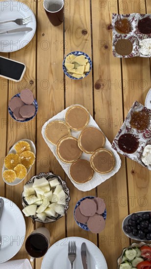 Wooden table spread of traditional moroccan breakfast, pancakes, sliced oranges and melon, olives, cucumber and tomato salad, cheeses, jams and butter in a colorful morning feast