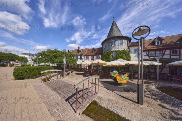 Altstadt, historische Fachwerkhäuser, Häuserzeile, hölzerne Fußgängerbrücke, Laterne, Turm, Gehweg aus Pflastersteinen und Betonpflastersteinen, Restaurant Zum Türmchen, Außenbereich einer Gastronomie mit Sonnenschirmen, Bäume, Hecke, blauer Himmel, Cumuluswolken, Cirrostratuswolken, Platz am Untertor, Burggrabenstraße, Hofheim am Taunus, Main-Taunus-Kreis, Hessen, Deutschland