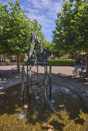 Brunnen mit Metallskulpturen, Alltägliches Theater, Bildhauer Hugo Uhl, Platz, Bäume, Hecke, blauer Himmel, Cirrostratuswolken, Burgstraße, Hofheim am Taunus, Main-Taunus-Kreis, Hessen, Deutschland